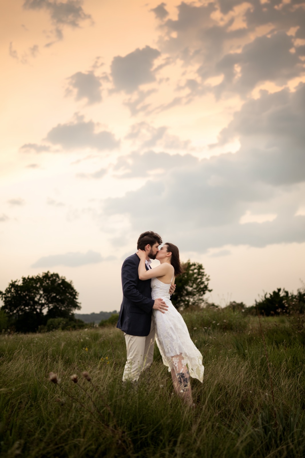 Engaged couple kissing in a Dallas field at golden-hour sunset